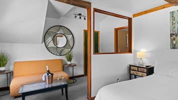Quarto de hotel com cama, sofá, mesa de centro com uma garrafa de champanhe, espelho e abajur.