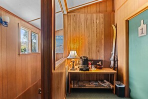 A compact room with wooden walls, a small table with a lamp, a coffee maker, and a ski rack. - Jessie's Harvest House Suite (Tannersville)