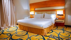 A hotel room with a large bed, a wooden headboard, two bedside lamps, and a patterned carpet. - Alsltanah Jazan Hotel (Jizan)