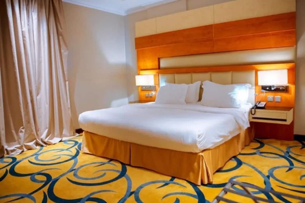 A hotel room with a large bed, a wooden headboard, two bedside lamps, and a patterned carpet.