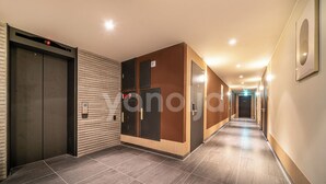 A modern hotel corridor with a wooden panel wall, a digital elevator display, and a tiled floor. - BROWN-DOT HOTEL (Busan)