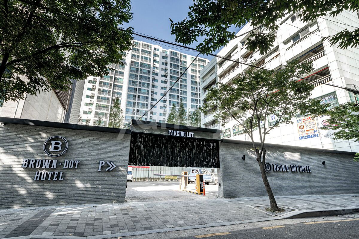 The entrance to Brown-Dot Hotel with a parking lot sign, a gated entrance, and a tree in the foreground.