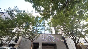 The exterior of the Brown-Dot Hotel with a modern glass facade, a parking entrance, and a tree-lined street. - BROWN-DOT HOTEL (Busan)