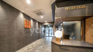A reception area with a marble floor, a reception desk with a round light, and a wall with a geometric pattern. - BROWN-DOT HOTEL (Busan)