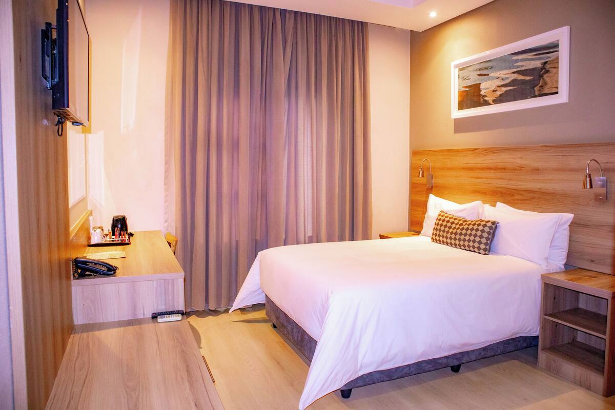 Een hotelkamer met een groot bed, een bureau met telefoon, een lamp en een schilderij aan de muur.
