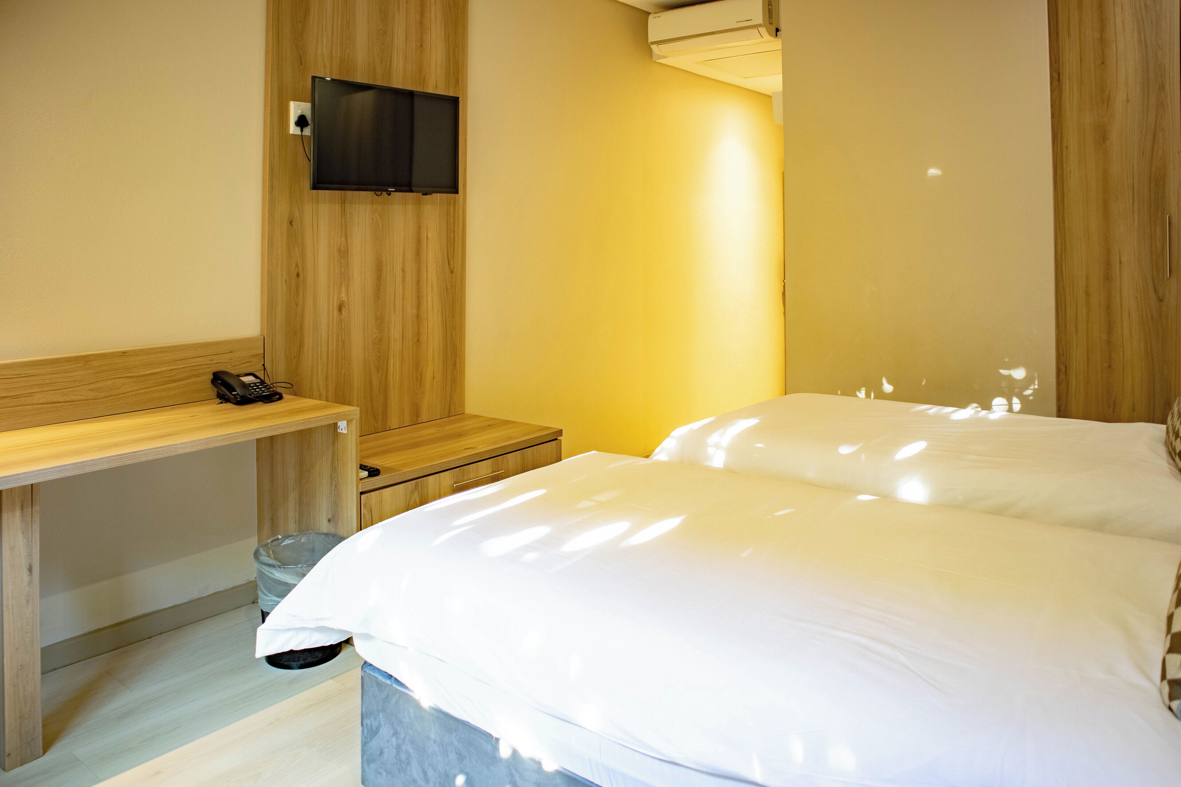 Habitación de hotel con un escritorio de madera, un televisor instalado en la pared y una cama con ropa blanca.