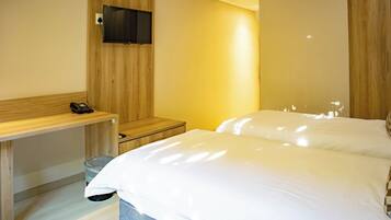 Habitación de hotel con un escritorio de madera, un televisor instalado en la pared y una cama con ropa blanca.