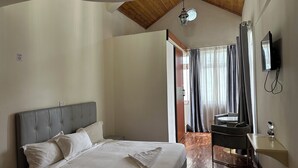Une chambre avec un grand lit, un plafond en bois, un bureau avec une chaise et un téléviseur fixé au mur.