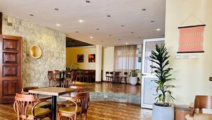 Un hall d’hôtel spacieux, doté de meubles en bois, d’un mur en pierre et de plantes en pot.