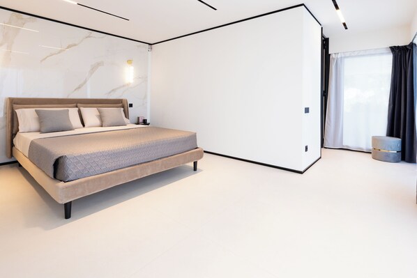 Une chambre moderne avec un grand lit, une table de chevet, une commode et une grande fenêtre avec des rideaux.