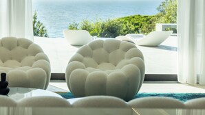 Una sala de estar moderna con vista al océano, que presenta sillones redondos tapizados y una mesa de vidrio.