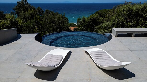Una piscina con dos sillas reclinables y vista al mar.