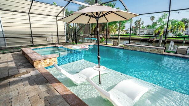 A swimming pool with a slide, lounge chairs, and an umbrella. - Resort-Style Canal Home w/ Pool & Putting Green - Baywatch (Apollo Beach)