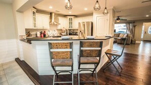 A modern kitchen with white cabinetry, a stainless steel refrigerator, and a bar area with two stools. - Resort-Style Canal Home w/ Pool & Putting Green - Baywatch (Apollo Beach)
