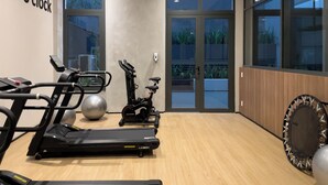 Een fitnessruimte met trainingsapparatuur, grote ramen en een houten vloer.