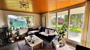 Ein gemütliches Zimmer mit Holzboden, einer Couch, einem Couchtisch und einem großen Fenster mit Blick auf den Garten.