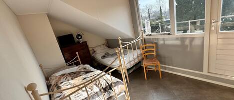 Une chambre de dortoir avec un lit superposé, une chaise en bois, une commode et une fenêtre donnant sur des arbres.