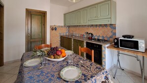 A dining area with a table set for two, a fruit bowl, and a microwave on the counter. - La Casetta Di Greise (Budoni)