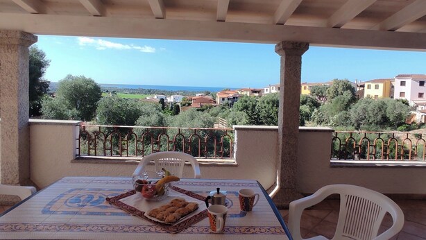A terrace with a table set for breakfast, overlooking a scenic view of houses and greenery. - La Casetta Di Greise (Budoni)
