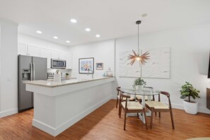 Une cuisine moderne avec des meubles blancs, un réfrigérateur en acier inoxydable, un four à micro-ondes et une machine à café.