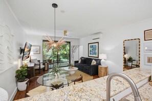 Un salon moderne avec une table basse en verre, un canapé foncé et un coin repas doté d’un comptoir en marbre.