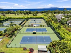 Un complexe de courts de tennis comprenant plusieurs terrains, entouré d’une végétation luxuriante et offrant une vue sur l’océan.