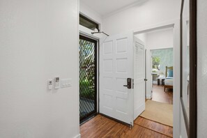 Un pasillo con una puerta blanca, una malla de seguridad negra, una pared blanca con un termostato y suelo de madera.