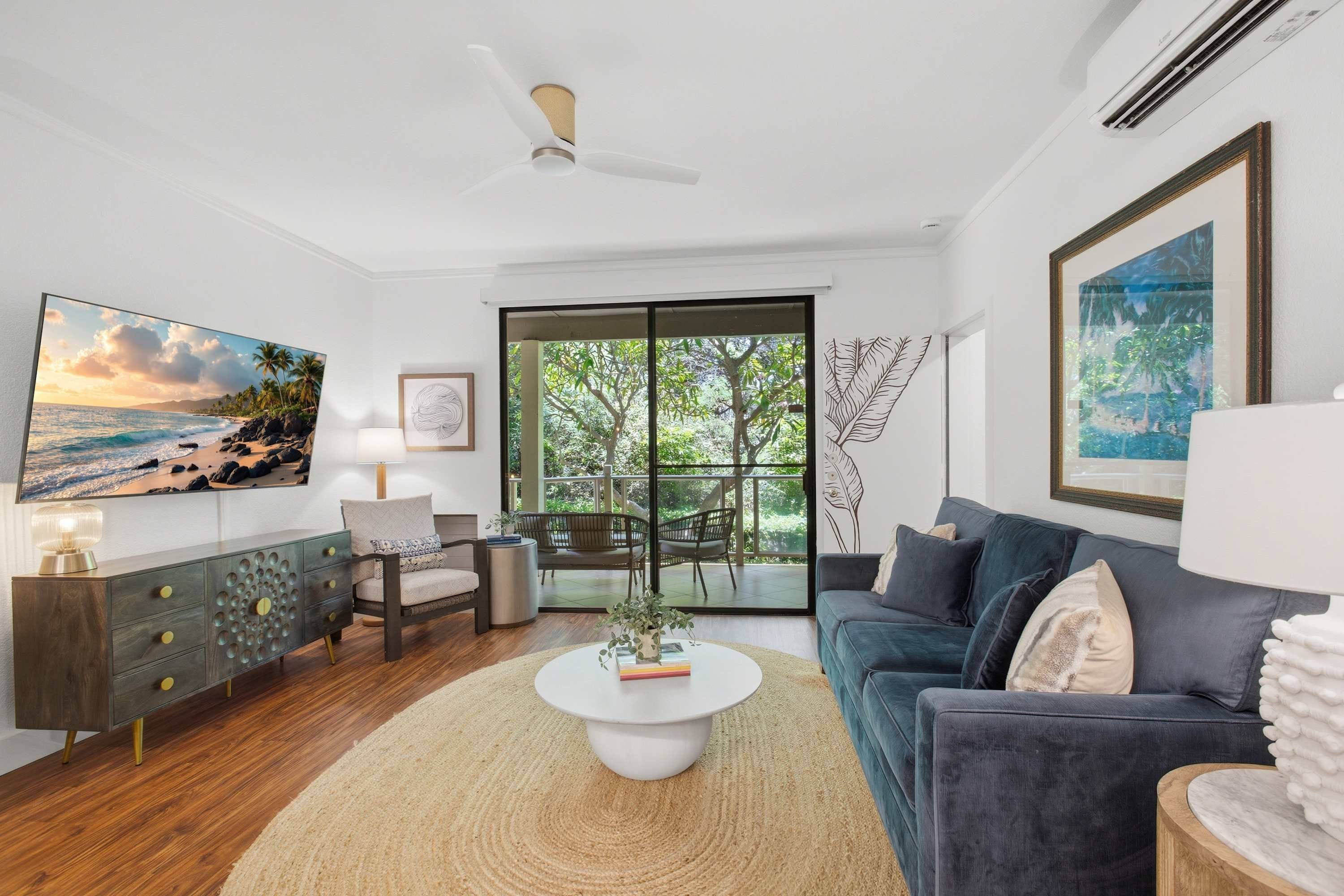 Una sala de estar moderna con un televisor grande, un sofá, una mesa de centro y vistas al exterior a través de un ventanal.