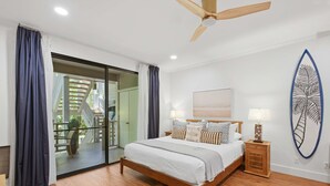 Una camera da letto con un letto, una ventola a soffitto, un comodino, una decorazione a forma di tavola da surf e vista attraverso una porta in vetro.