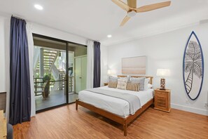 A bedroom with a bed, a ceiling fan, a nightstand, a surfboard decoration, and a view through a glass door. - Newly Remodeled! Wailea 2BR | Walk to Beach | A/C | Family-Friendly (Kihei)