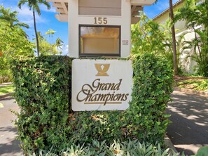 L’entrée d’un immeuble, avec une enseigne indiquant « Grand Champions » et le numéro « 155 » au-dessus.