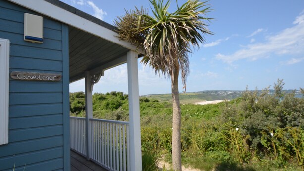 A coastal building with a porch, a palm tree, and a view of the beach. - C14 Gwelmore, Riviere Towans (Hayle)