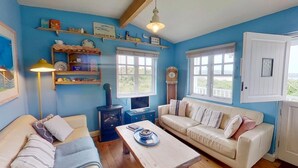 A cozy room with a blue wall, a white sofa, a wooden coffee table, and a lamp. - C14 Gwelmore, Riviere Towans (Hayle)