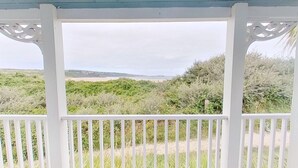A view through a white wooden gate with intricate designs, leading to a natural landscape with dense greenery and a distant beach. - C14 Gwelmore, Riviere Towans (Hayle)