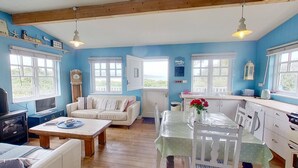 A cozy room with a sofa, a dining table, and a kitchen area with a sink and stove. - C14 Gwelmore, Riviere Towans (Hayle)
