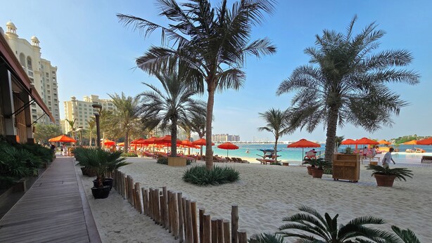 A beach area with wooden walkways, palm trees, and red umbrellas. - Highend Azure Stay In Palm Jumeirah (Dubai)