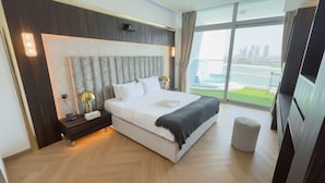 A modern hotel room with a large bed, a nightstand, a lamp, and a view of a city skyline through large windows. - Highend Azure Stay In Palm Jumeirah (Dubai)