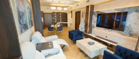 A modern living room with a white sofa, blue armchairs, a coffee table, and a TV mounted on a marble wall.