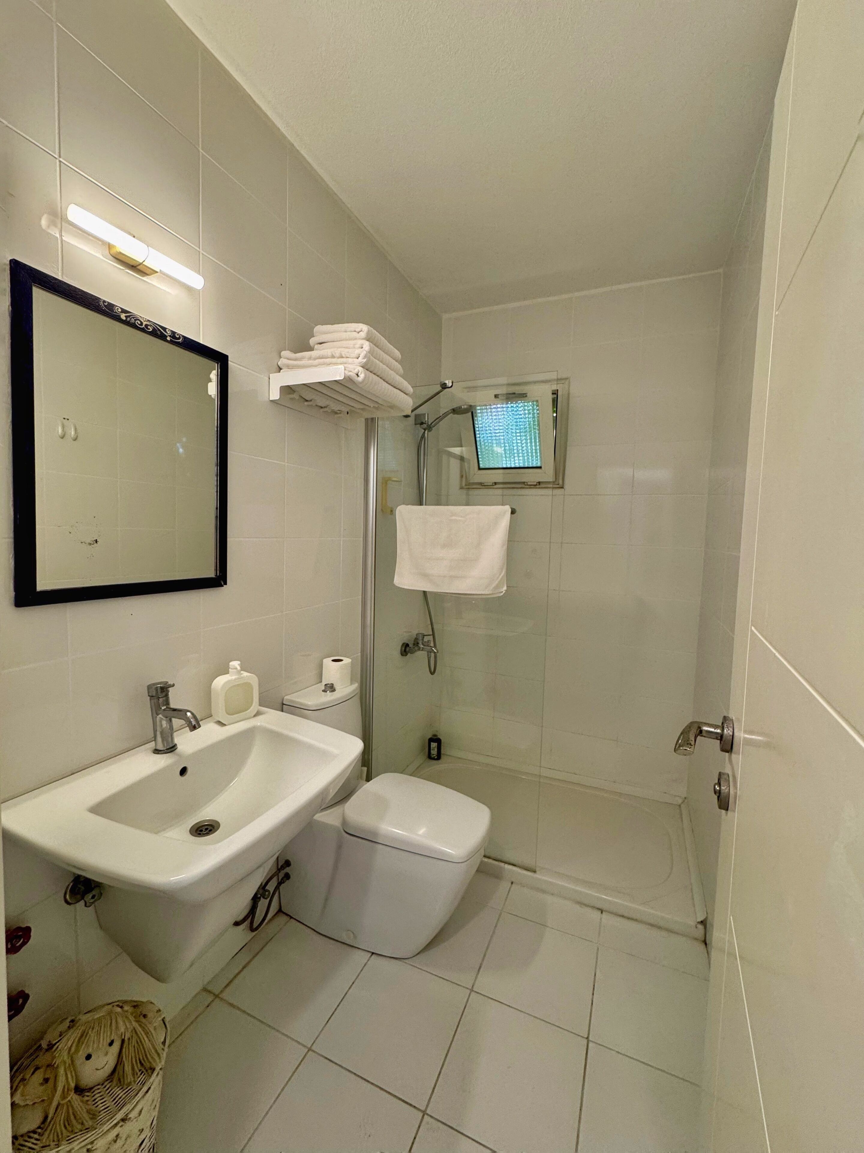 A small, clean bathroom with a sink, toilet, and shower. There is a mirror above the sink and a towel rack with towels.