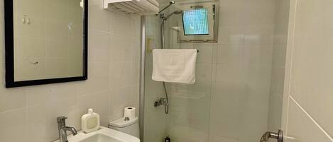 A small, clean bathroom with a sink, toilet, and shower. There is a mirror above the sink and a towel rack with towels.