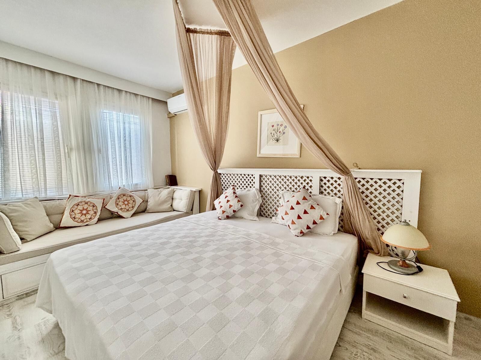 A bedroom with a large bed, a bedside table, a nightstand, and a window with curtains.