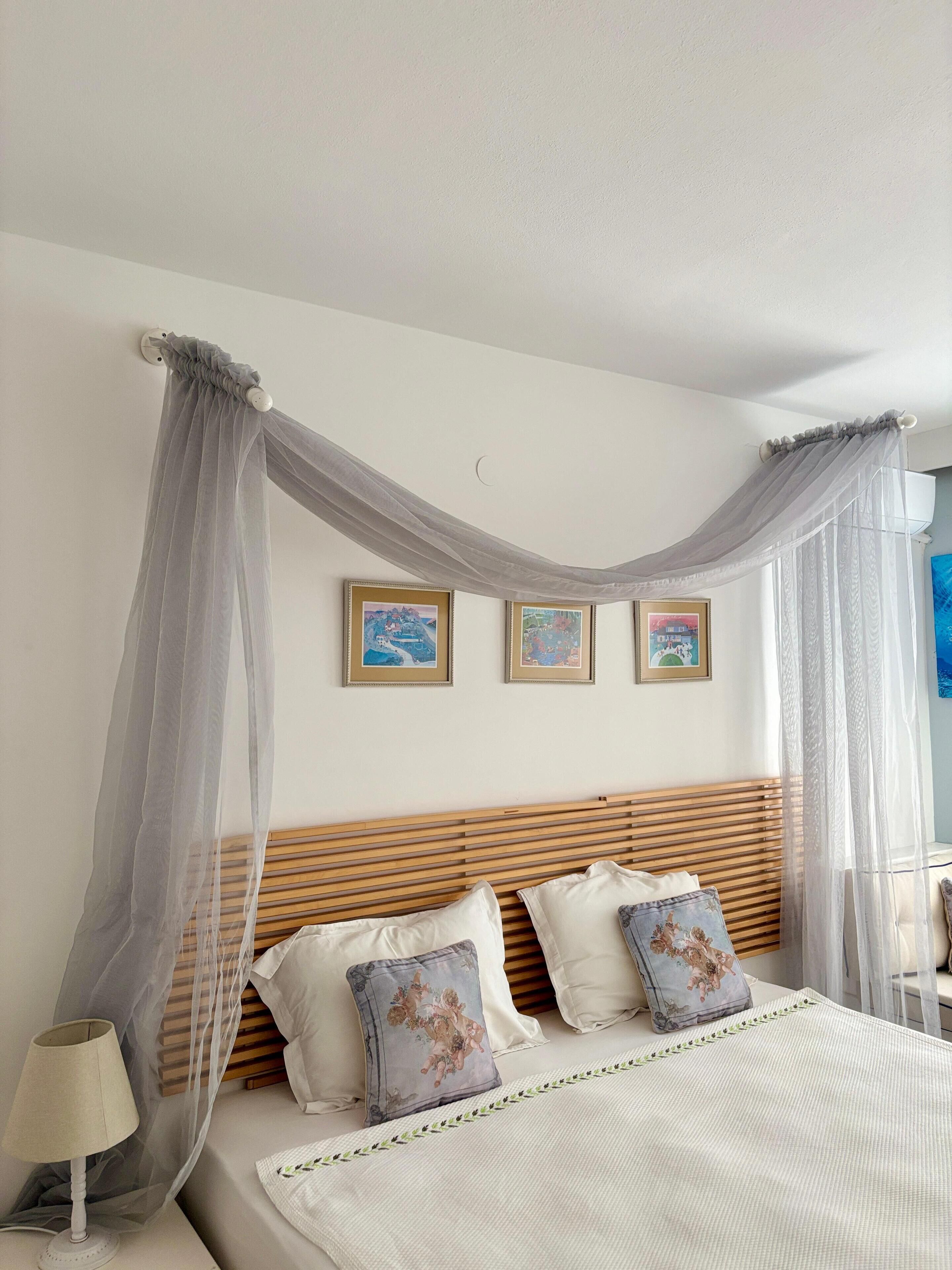 A bedroom with a canopy bed, wooden headboard, and three framed pictures on the wall.