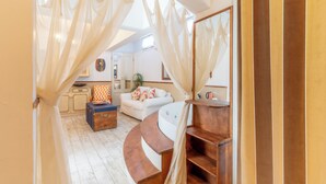 A cozy room with a curved wooden bench, a white sofa, and a small table. There is a large mirror on the wall and a window with sheer curtains. - Mon Ilıca Otel (Cesme)