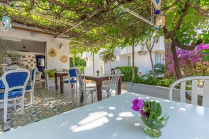 An outdoor dining area with white tables and chairs, surrounded by greenery and a pergola. - Mon Ilıca Otel (Cesme)
