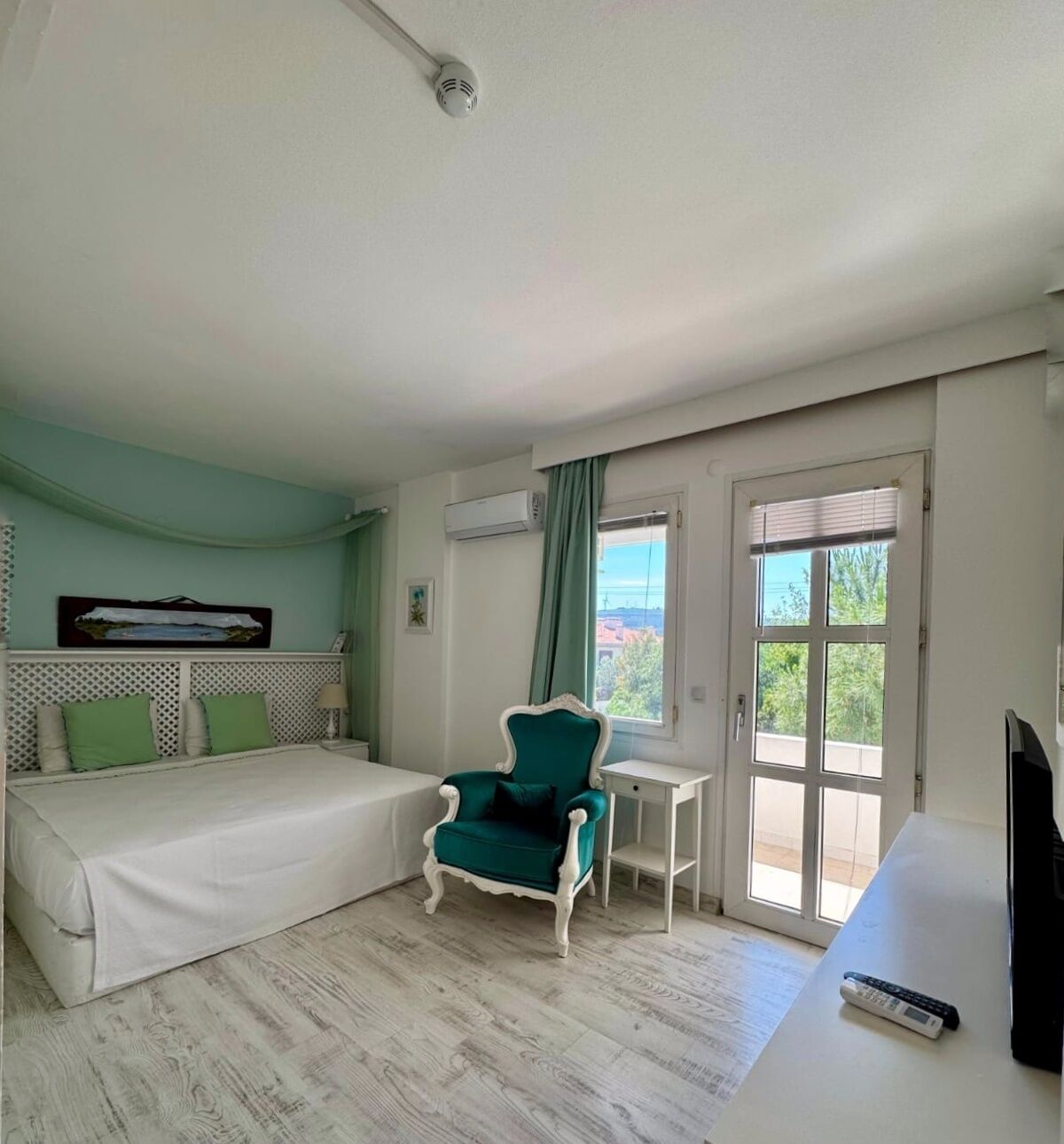A bedroom with a bed, a green armchair, a small table, and a TV.