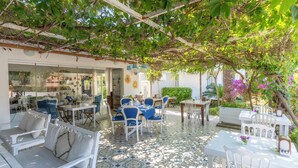 An outdoor patio with white furniture, a tiled floor, and a pergola covered with greenery. - Mon Ilıca Otel (Cesme)