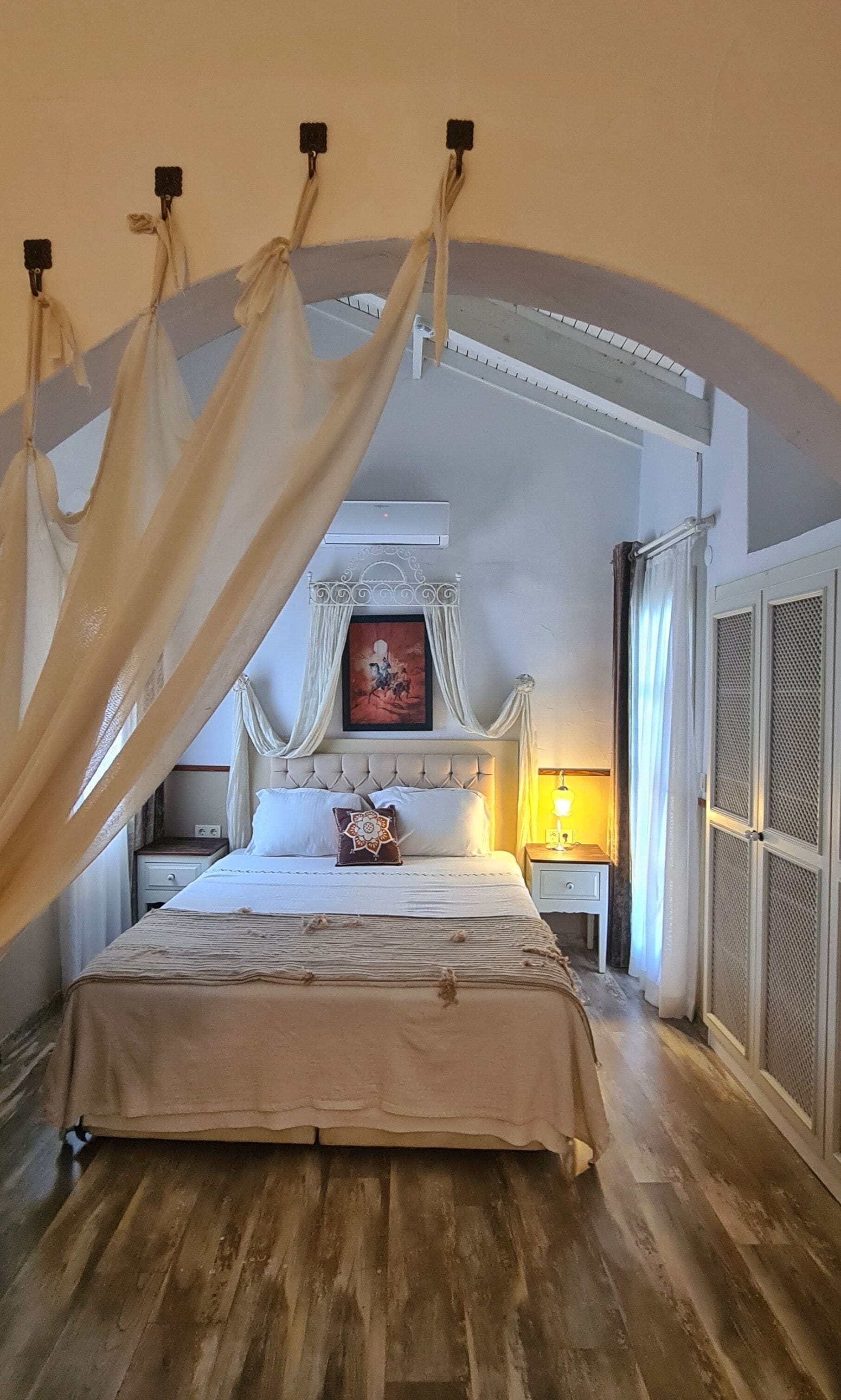 Een slaapkamer met een bed, nachtkastje, lamp en een raam met gordijnen.