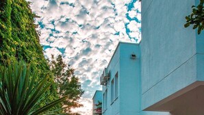 A narrow pathway leading to a building with a blue facade, surrounded by lush greenery and flowering plants. - Mon Ilıca Otel (Cesme)