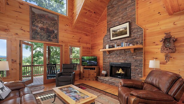 Ein gemütliches Blockhaus-Interieur mit Kamin, Ledermöbeln und einem großen Fenster mit Blick auf einen Wald.