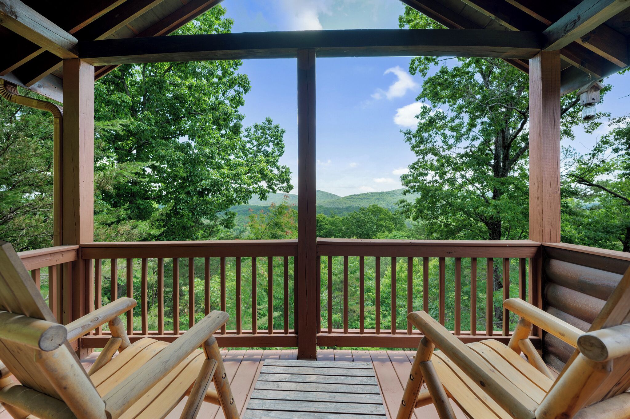 A wooden deck with two wooden chairs facing a scenic view of a forested landscape.